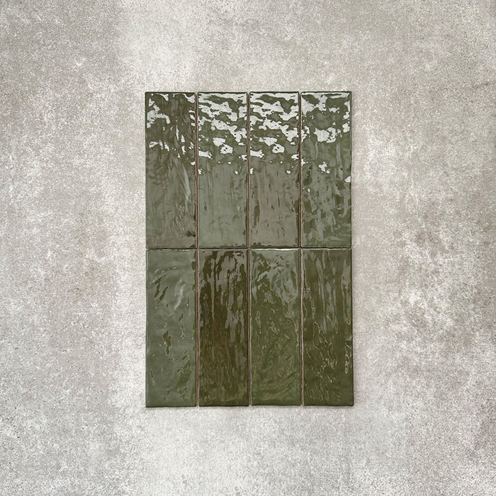 Flatlay von Zellige Botanisches Grün Ziegel Keramikfliesen im marokkanischen Stil im Format 6,5 × 20 cm, in tiefen botanischen Grüntönen. Vertikal im Ziegelverband auf strukturiertem grauem Hintergrund arrangiert, um die glänzende Glasur, die natürliche Farbvariation und die handgefertigte Zellige-Optik zu zeigen.