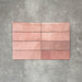 Flatlay von Zellige Rosa Brick Keramikfliesen im marokkanischen Stil im Format 6,5 × 20 cm, in sanften Blush-, Altrosa- und Terrakotta-Pinktönen mit feiner tonaler Variation und leicht unregelmäßigen Kanten. Vertikal im Ziegelverband auf strukturiertem grauem Hintergrund arrangiert, um die handwerkliche Zellige-Optik zu zeigen.