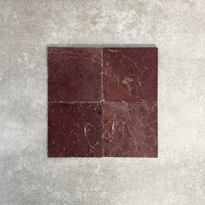 Vier Fayrouz Bordeaux 15,2 × 15,2 cm Naturmarmorfliesen mit getrommelter Oberfläche nebeneinander angeordnet, die satten Rottöne, natürliche Maserung und Oberflächenvariation vor einem neutralen, strukturierten Hintergrund zeigen.