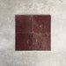 Vier Fayrouz Bordeaux 15,2 × 15,2 cm Naturmarmorfliesen mit getrommelter Oberfläche nebeneinander angeordnet, die satten Rottöne, natürliche Maserung und Oberflächenvariation vor einem neutralen, strukturierten Hintergrund zeigen.