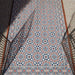 Außenbereich mit Berlin Großartig Bodenfliesen im Format 20 × 20 cm im viktorianisch-marokkanisch inspirierten Stil. Das feine geometrische Muster in Marineblau, Terrakotta und Weiß wird durch schwarze Geländer und natürliches Sonnenlicht stilvoll ergänzt.